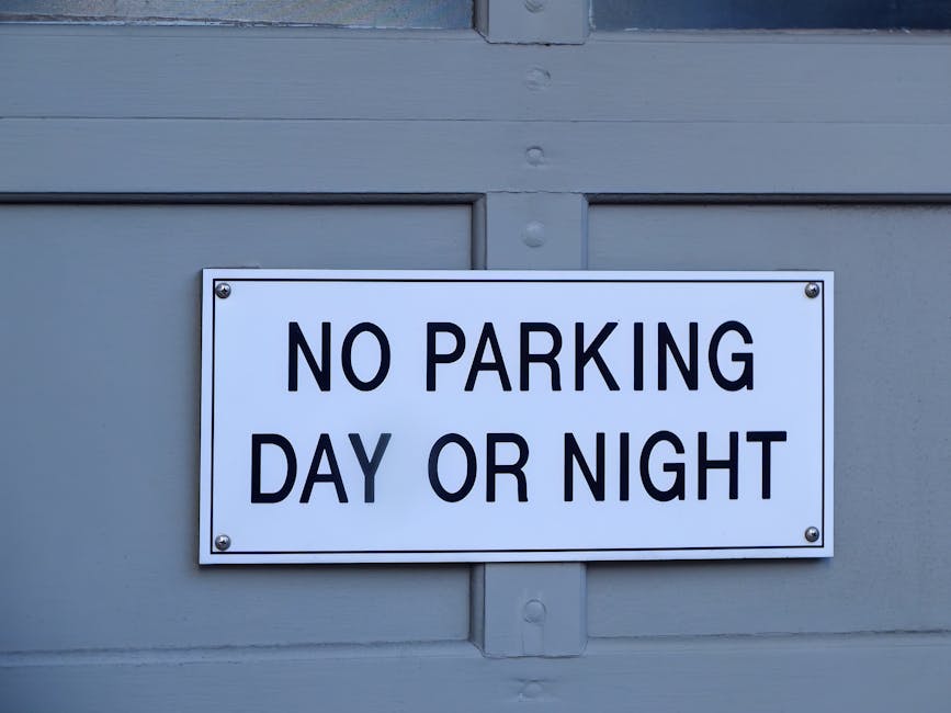 A circular traffic sign with a white background, featuring a bold black letter 'P' crossed out by a thick red line, indicating no parking. The sign is mounted on a silver metal pole situated outdoors